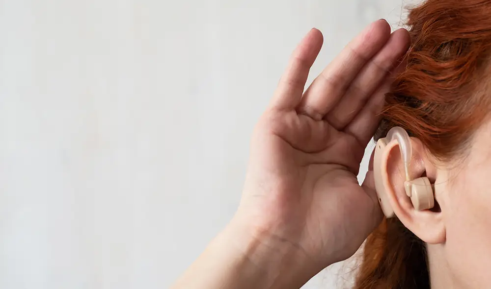 A hand cupped over an ear with a hearing aid
