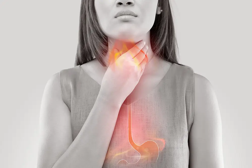 A woman clutching her throat with an illustration of an inflamed esophagus overlaying the photo, illustrating acid reflux