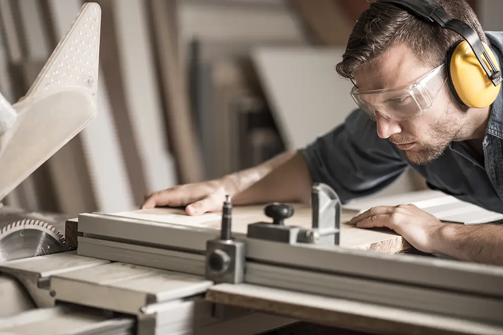 A man wearing hearing and eye protection while operating a table saw