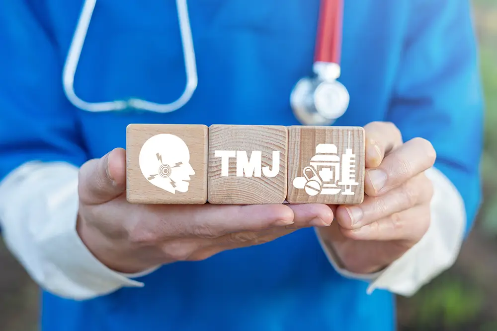 A doctor holding wooden blocks that read "TMJ"
